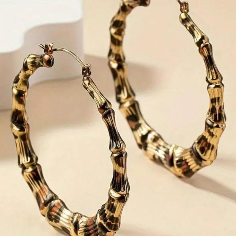 May include: Gold hoop earrings with a leopard print design. The earrings are made of a bamboo-like material.