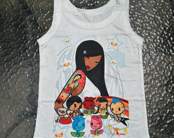 May include: White tank top featuring a graphic of a woman with long black hair and a tattoo on her arm, surrounded by cartoon characters, stars, and roses. The design includes the text "tokidoki".