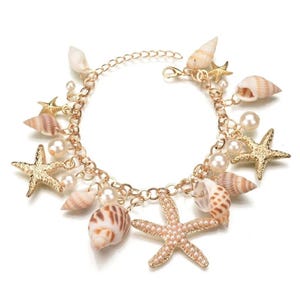 May include: Gold chain bracelet with multiple charms, including seashells, starfish, and pearls. The charms are in shades of brown, white, and gold.