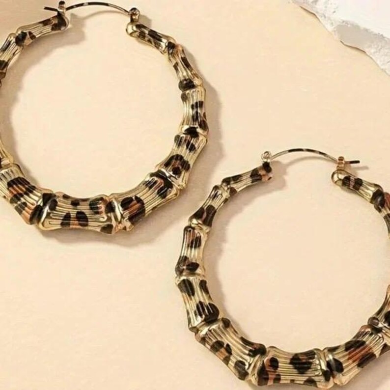 May include: A pair of gold hoop earrings with a leopard print design. The earrings are made of a bamboo-like material.