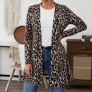 Puede incluir: Cárdigan largo con estampado de leopardo en marrón y negro, con la parte delantera abierta. Se lleva sobre una camiseta blanca y vaqueros azules, con un cinturón negro. Las mangas son largas y el cárdigan llega a la mitad del muslo.