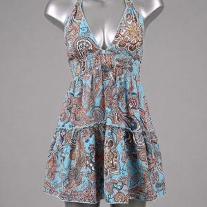 May include: A light blue halter-neck mini dress featuring a detailed paisley print in shades of brown, white, and dark blue. The garment has a deep V-neckline, an elasticized empire waist, and a tiered skirt with a ruffled hemline finish.