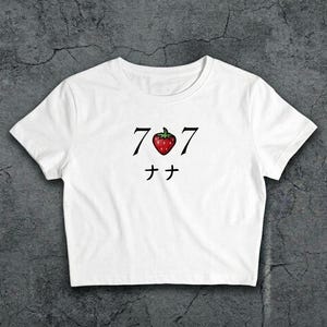May include: White crop top with a graphic design. The design features the numbers "707" in black, with a red strawberry in the centre. Below the numbers are two Japanese characters. The shirt is made of a soft material.