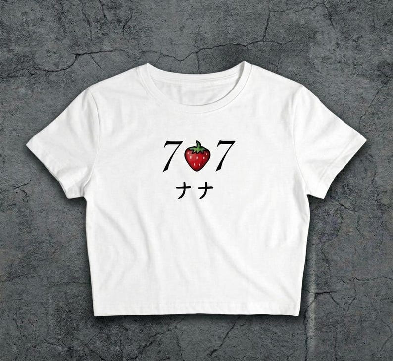May include: White crop top with a graphic design. The design features the numbers "707" in black, with a red strawberry in the centre. Below the numbers are two Japanese characters. The shirt is made of a soft material.