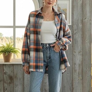 May include: A plaid button-down shirt in orange, blue, black, and white is worn over a white tank top and blue jeans. The shirt has long sleeves and a collared neckline. The jeans are a light wash denim. The outfit is casual and stylish.