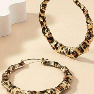 May include: A pair of large gold hoop earrings with a leopard print design. The earrings are made of metal and have a bamboo-like texture.