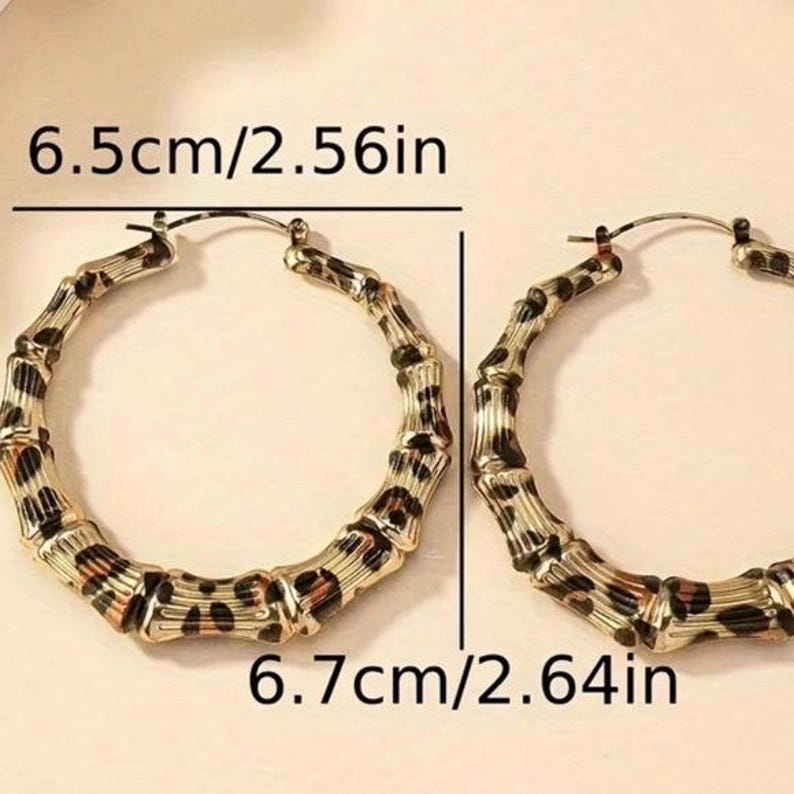May include: A pair of large gold hoop earrings with a leopard print design. The earrings measure 6.5 cm/2.56 inches in diameter and 6.7 cm/2.64 inches in diameter.