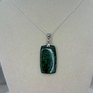 May include: A silver chain necklace with a green stone pendant. The pendant is rectangular and has a smooth, polished surface.