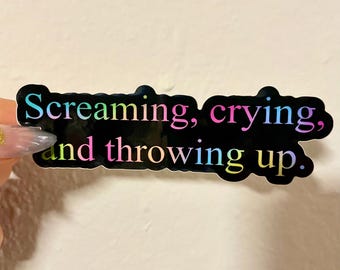 Peut inclure: Autocollant noir avec le texte "Screaming, crying, and throwing up." Le texte est dans un dégradé arc-en-ciel. L'autocollant a une bordure noire et est tenu par une main.