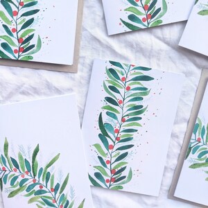 May include: A collection of white greeting cards featuring a watercolor illustration of a vertical green leafy branch with small red berries. The design includes delicate light blue foliage accents and scattered red dots on a clean white background.