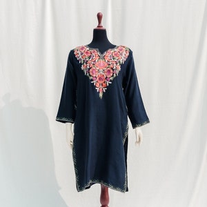 May include: A navy blue tunic with a floral embroidery design on the neckline. The tunic is displayed on a mannequin against a white backdrop.