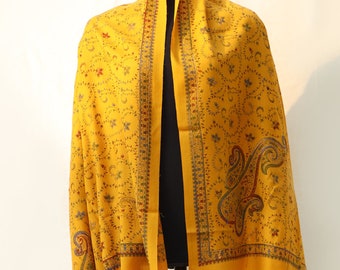 May include: A yellow shawl with a paisley pattern and floral embroidery. The shawl is draped over a mannequin.