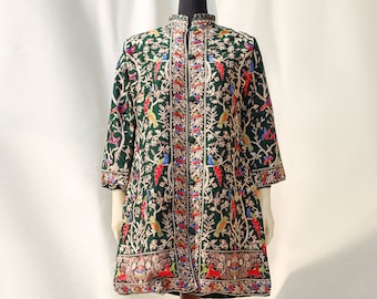 May include: A dark green, long-sleeved coat with a mandarin collar, displayed on a mannequin. The coat is intricately embroidered with colorful birds, flowers, and foliage. The embroidery includes red, blue, yellow, and white accents.