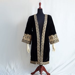 Op de afbeelding: Een zwarte fluwelen kimono met gouden borduurwerk. De kimono heeft een lange, open voorkant en wijde mouwen. Het borduurwerk is ingewikkeld en heeft bloem- en geometrische patronen.