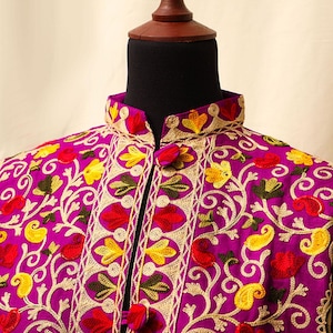Peut inclure: Une veste brodée violette avec un col mandarin et des motifs floraux dans des tons de rouge, jaune et vert.