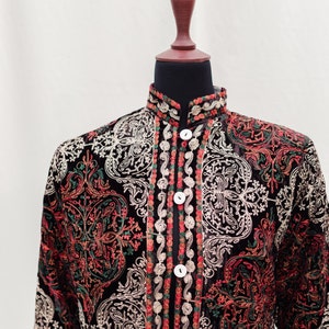 May include: A black velvet jacket with intricate embroidered floral patterns in shades of red, green, and white. The jacket has a mandarin collar and a button closure.