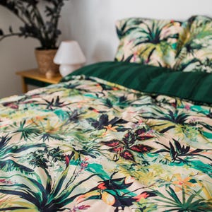 May include: A tropical-themed bedding set with a cream background and a vibrant green, blue, and yellow print of palm leaves and toucans. The set includes a duvet cover and two pillowcases.