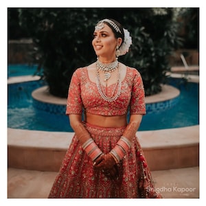 Bridal red hand embroidered Indian wedding lehenga with floral jal embellished blouse paired with peach and red dupatta.