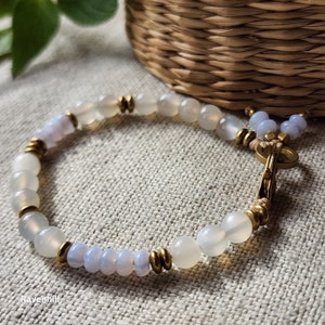 May include: A white and blue beaded bracelet with gold accents. The bracelet has a clasp closure and is made with natural stones.