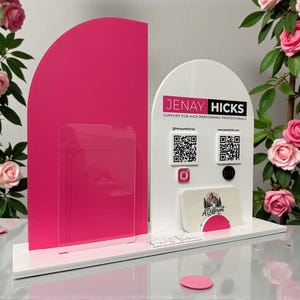 May include: A white and pink display stand with the text "JENAY HICKS" and social media icons. The stand features a clear acrylic panel and a slot for business cards. Pink rose blossoms are in the background.