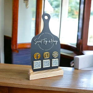 May include: Black chalkboard sign with a gold inscription that reads "Premium Ingredients Sweet Fig & Honey Stunning Presentation". The sign has a wooden base and features four gold square buttons with QR codes and social media icons.