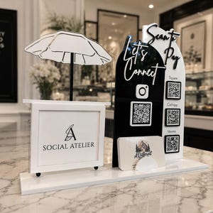 May include: A white and black acrylic sign stand featuring a cutout umbrella shape, a frame with the text SOCIAL ATELIER, and an arched panel with the text Let's Connect and Scan to Pay. It includes QR codes for Square, Cashapp, and Venmo.