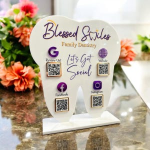 May include: A white tooth-shaped sign with the text "Blessed Smiles Family Dentistry" and the phrase "Let's Get Social".  The sign has four QR codes for Google, Facebook, Instagram, and Website.