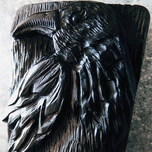 Puede incluir: Escultura de cuervo negro tallada, con texturas detalladas de plumas y pico. La cabeza del cuervo se destaca, mostrando la intrincada artesan&iacute;a de la obra de arte. La escultura tiene una apariencia r&uacute;stica y artesanal.