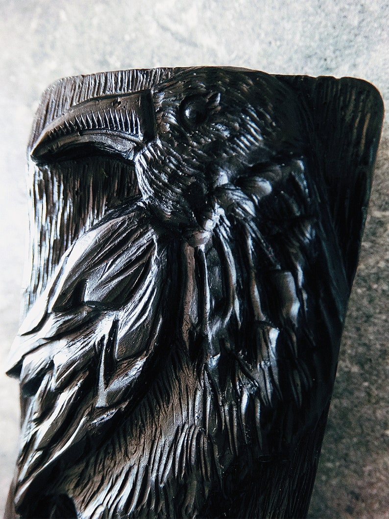 Puede incluir: Escultura de cuervo negro tallada, con texturas detalladas de plumas y pico. La cabeza del cuervo se destaca, mostrando la intrincada artesan&iacute;a de la obra de arte. La escultura tiene una apariencia r&uacute;stica y artesanal.