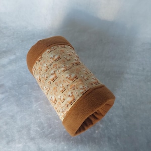Può includere: Un tunnel in tessuto cilindrico con un pannello centrale color crema caratterizzato da un motivo ripetitivo di piccole pecore e alberi marroni, fiancheggiato da estremità in pile marrone tinta unita. L'oggetto tubolare morbido è cavo.