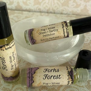May include: Three roll-on perfume bottles with black caps and labels that read "Forks Forest" and "Forest". The labels also state "Fog + Moss Green + Earthy Petrichor". The bottles are .33oz/10ml. The bottles are on a white bowl.