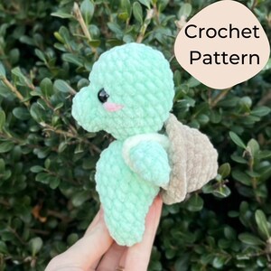 May include: A crocheted green turtle amigurumi toy with a brown shell. The toy has a cute face with black eyes and pink cheeks. Crochet Pattern.