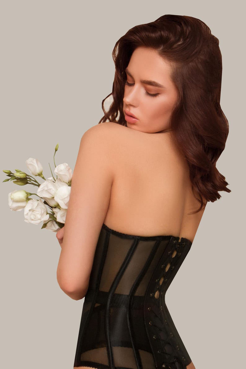 May include: A black corset with a lace-up back and a mesh panel. The corset is worn by a person with long brown hair.