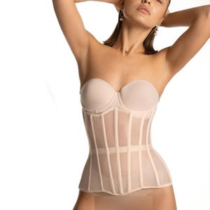 May include: A nude-colored mesh corset with boning and a scalloped hem. The corset is worn over a strapless bra.