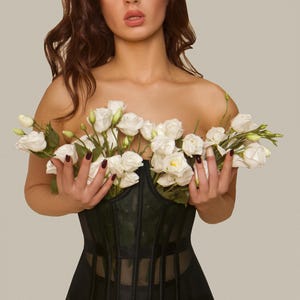 May include: A black corset with a mesh panel and a floral bouquet of white flowers.