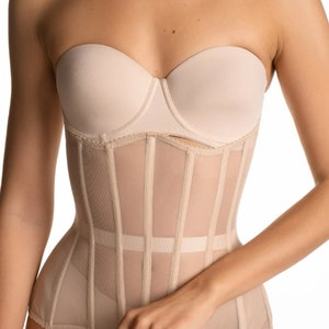 May include: A nude-colored mesh corset with a boned structure and a strapless bra underneath. The corset has a delicate, sheer fabric and a fitted silhouette.