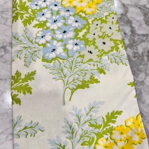 May include: White fabric with a floral pattern featuring blue, yellow, and green flowers. The fabric has a vintage feel and would be perfect for a tablecloth, curtains, or upholstery.