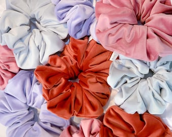 Può includere: Una collezione di scrunchies colorati in varie tonalità di blu, rosa e rosso. Gli scrunchies sono realizzati in tessuto morbido e vellutato e sono perfetti per aggiungere un tocco di stile a qualsiasi acconciatura.