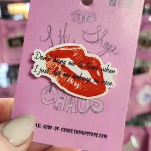 May include: A pink card with a red lip sticker and the text "Don't bring me to tears when I just did my makeup so nice." The card also has the words "Lil Shop of Chaos" and a website address.