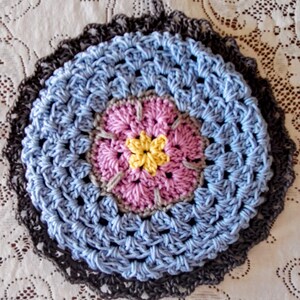 May include: A crocheted doily with a blue, pink, and yellow center. The doily has a dark gray border.