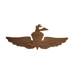 Peut inclure: Insigne militaire de couleur bronze, avec un emblème central représentant un oiseau stylisé et un parachute, flanqué d'ailes déployées. L'emblème est probablement un badge ou un insigne pour une unité militaire ou une réalisation spécifique.