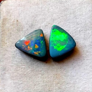 May include: Two triangular-shaped loose opals with a dark base colour. The left opal displays flashes of red, orange, and blue, while the right opal features a prominent, vibrant green play-of-colour across its polished, smooth surface.
