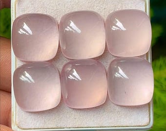 May include: Six pale pink, square-cut gemstones are displayed in a white tray. The stones have rounded corners and a smooth, polished surface. The gemstones are a soft, translucent pink colour.