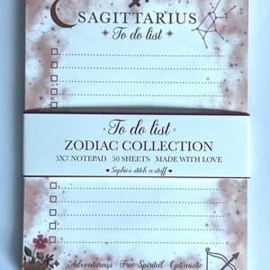 May include: A 5x7 notepad with a Sagittarius zodiac theme, featuring a brown watercolour background, a constellation, and a crescent moon. The text reads Sagittarius To do list, Zodiac Collection, 50 sheets, and Adventurous Free-Spirited Optimistic.