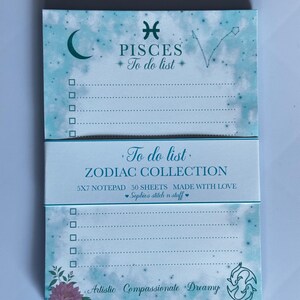 Peut inclure: Un bloc-notes bleu clair sur le thème des Poissons de 5x7 pouces avec 50 feuilles. La partie supérieure présente un croissant de lune, le symbole des Poissons et le texte "PISCES To do list". La partie inférieure inclut une fleur de lotus, le symbole des poissons et le texte "Artistic Compassionate Dreamy". Une bande centrale affiche "To do list ZODIAC COLLECTION 5X7 NOTEPAD 50 SHEETS MADE WITH LOVE Sophie's stitch n stuff".