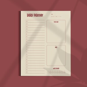 May include: A beige daily planner with a red border and text. The planner includes sections for time slots, a to-do list, notes, and a water tracker. The words "Daily Planner" are at the top in a decorative font.