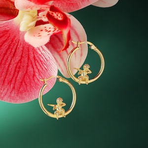 May include: Gold hoop earrings with a small cherub figure on each hoop.
