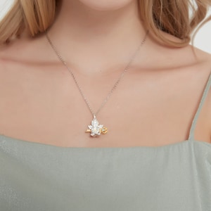 Op de afbeelding: Een zilveren ketting met een delicate hanger met een gestileerde engel die een sleutel vasthoudt. De engel is gemaakt van zilver en goud, en de sleutel is van goud. De hanger heeft een kleine blauwe edelsteen.