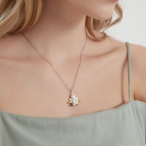 Op de afbeelding: Een zilveren ketting met een zilveren en gouden hanger met een gedetailleerd bloemmotief. De hanger heeft een kleine groene edelsteen in het midden.