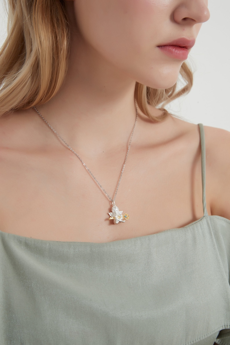 Op de afbeelding: Een zilveren ketting met een zilveren en gouden hanger met een gedetailleerd bloemmotief. De hanger heeft een kleine groene edelsteen in het midden.